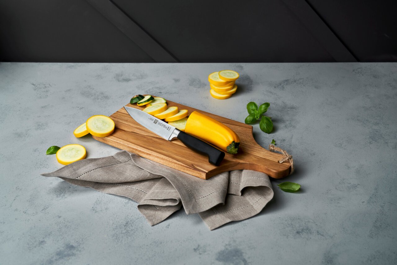 Fleischmesser 16cm VIER STERNE auf einem Holzbrett mit geschnittenem gelbem Gemüse, seitliche Perspektive