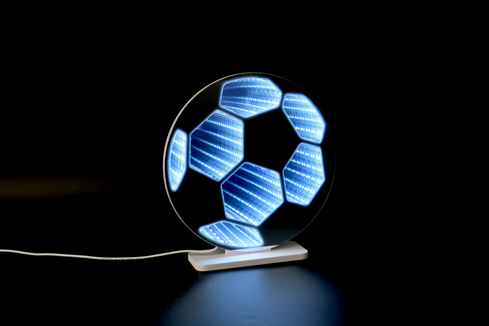 Leuchtende LED-3D-Lampe in Form eines Fußballs mit blauem Infinity-Spiegel-Effekt auf weißem Sockel, schräg von vorn auf schwarzem Hintergrund fotografiert