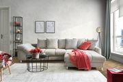 Gemütliche Rundecke in einem modernen Wohnzimmer, frontal betrachtet, mit hellgrauem Stoffbezug, dekoriert mit roten Kissen und Decke.