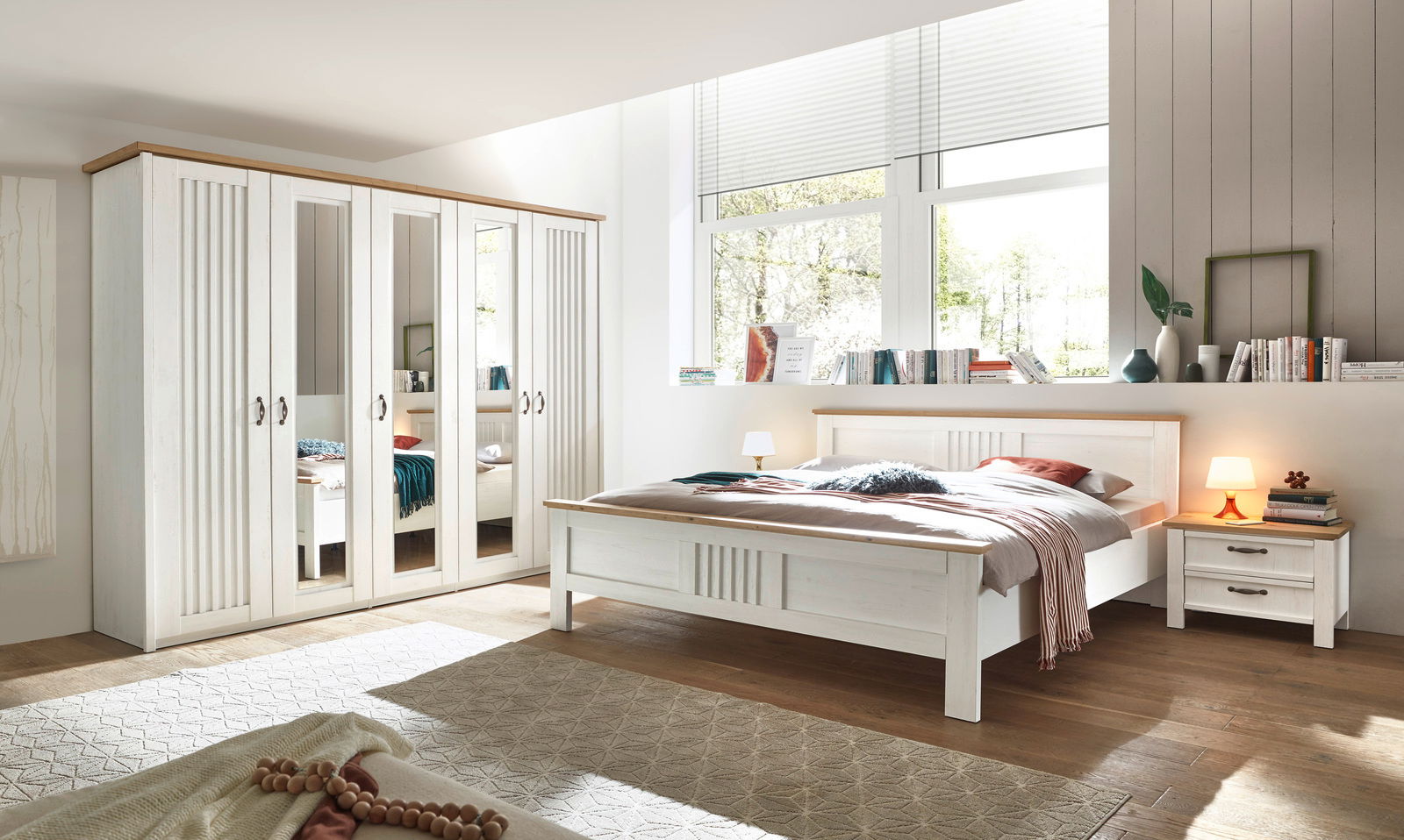 Helles Schlafzimmer mit weißem Kleiderschrank mit Spiegeln, einem Doppelbett und einem Nachttisch, aus der Perspektive von der Zimmerecke aus gesehen.