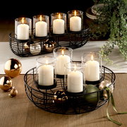 Dekokranz mit schwarzen Metallrahmen, weißen Kerzen in Glaszylindern und goldenen Kugeln, aus der Vogelperspektive fotografiert.