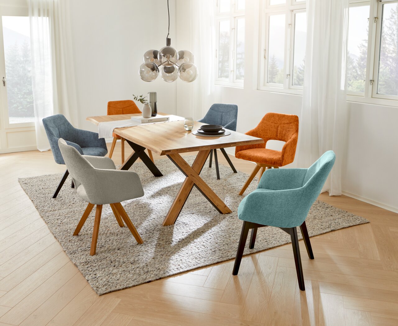 Voleo Fauteuil EVITA Eetkamer met een moderne houten tafel en diverse kleurrijke fauteuils, gefotografeerd vanuit een iets hoger standpunt.