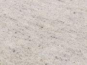 Nahaufnahme eines cremefarbenen Wollteppichs mit feiner Textur und vereinzelten dunklen Fasern, von oben betrachtet.