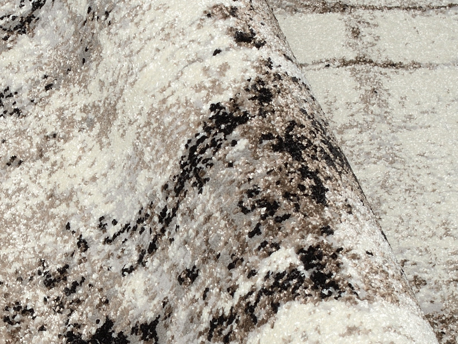 Nahaufnahme eines Designer-Teppichs mit abstraktem Muster in Beige- und Brauntönen, perspektivisch von der Seite aufgenommen.