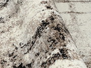 Nahaufnahme eines Designer-Teppichs mit abstraktem Muster in Beige- und Brauntönen, perspektivisch von der Seite aufgenommen.