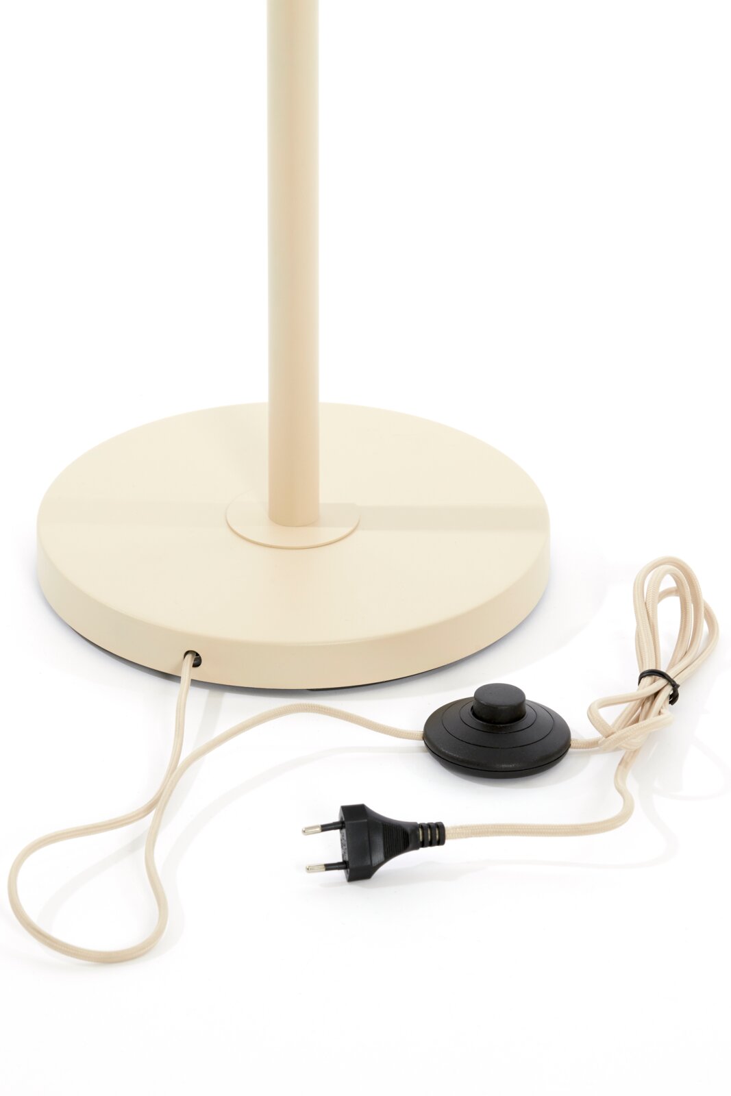 Close-up van de voet van een staande lamp met een ronde, beige voet en een zwarte voetschakelaar, gezien vanaf de zijkant.