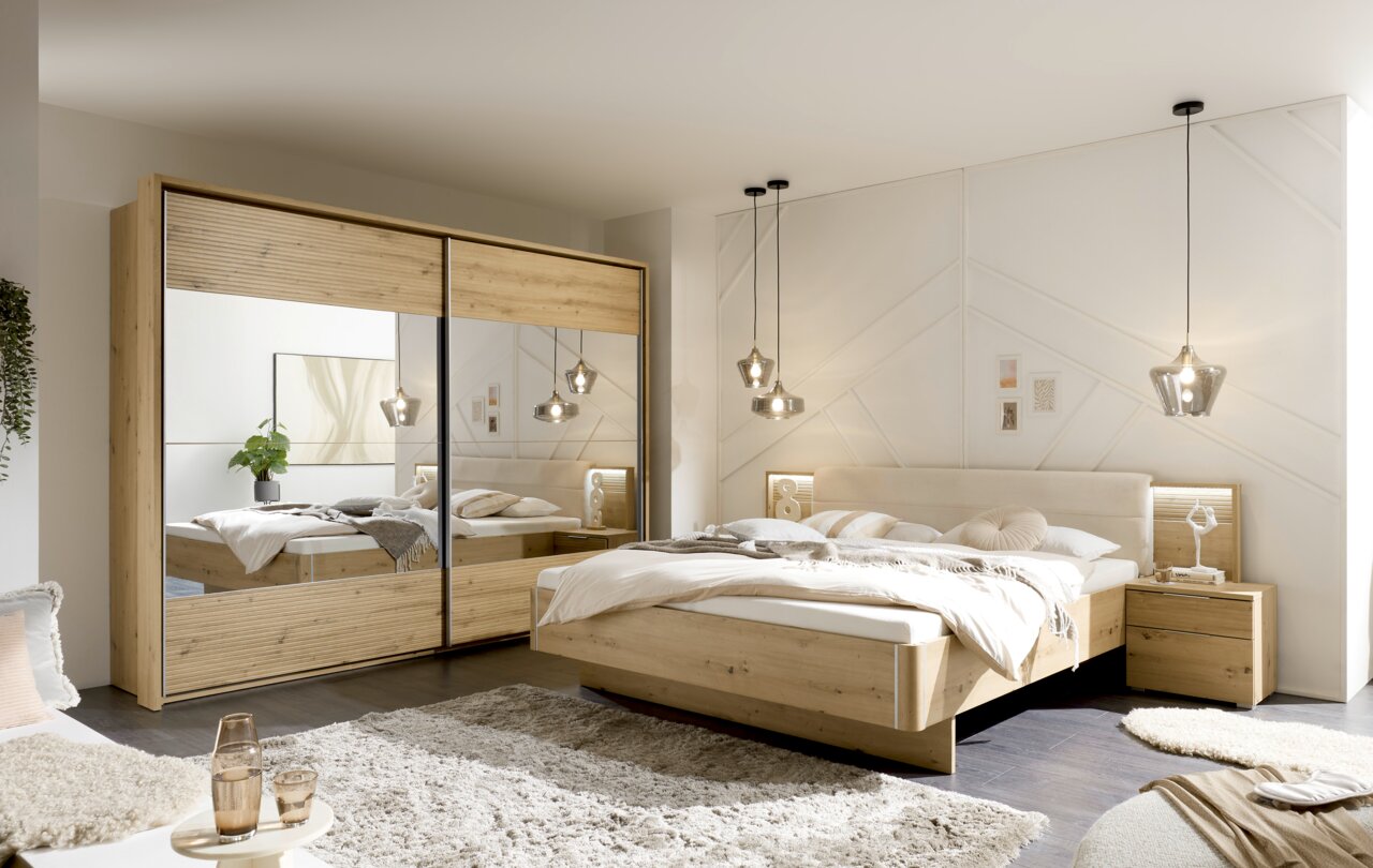 Modernes Schlafzimmer mit einem großen Kleiderschrank mit Spiegeltüren und einem gemütlichen Doppelbett aus Holz, seitliche Perspektive.