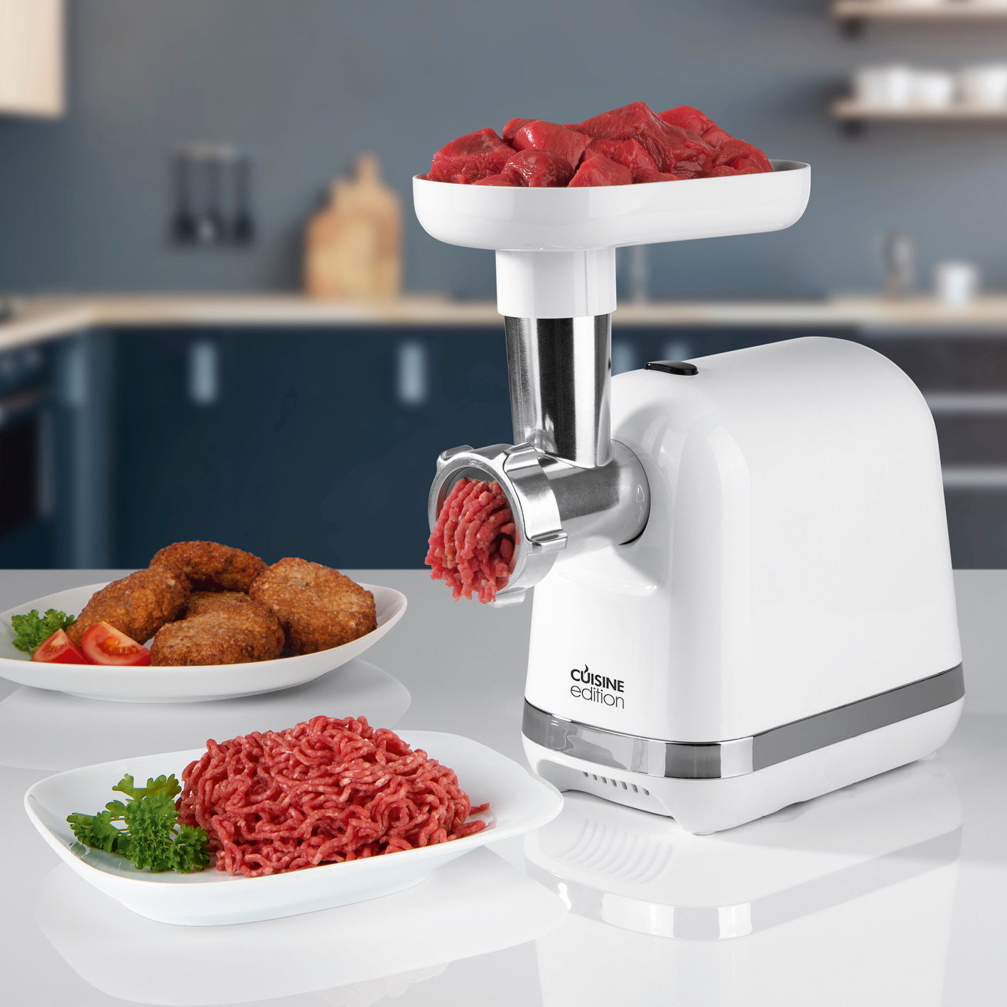 Fleischwolf der Marke Cuisine Edition in einer modernen Küche, seitliche Perspektive, mit frischem Hackfleisch und Fleischstücken auf einem Teller.