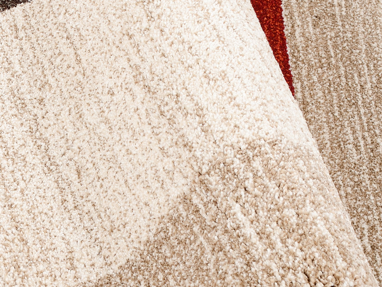 Nahaufnahme eines strukturierten Teppichs in Beige- und Brauntönen mit einem Hauch von Rot, perspektivisch von oben fotografiert.