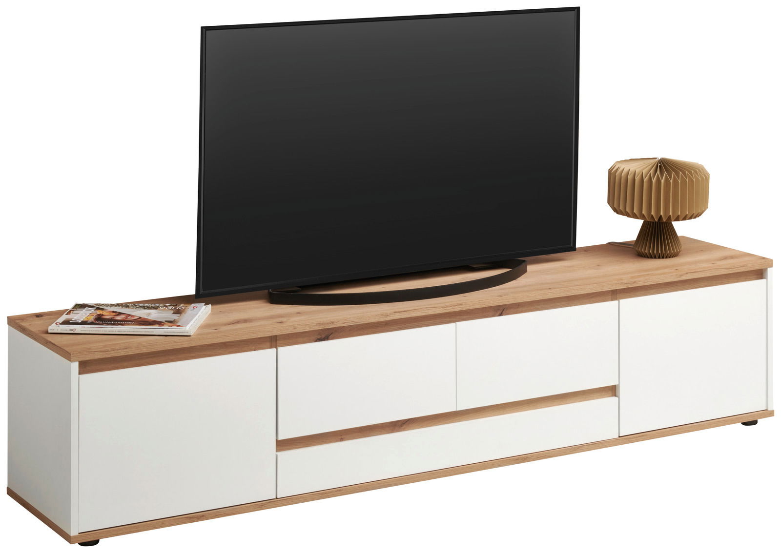 XL-TV-Lowboard in moderner Frontansicht mit weißem Korpus und Holzoberfläche, dekoriert mit einem Fernseher, einer Lampe und Zeitschriften.