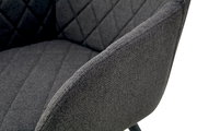 Nahaufnahme eines dunkelgrauen, gepolsterten Stoffstuhls mit gesteppter Rückenlehne und Armlehne, schräg von vorne/rechts fotografiert