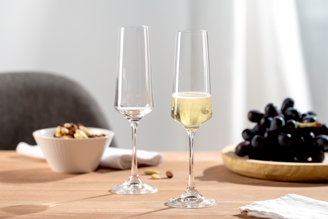 Leonardo Sektglas 6er-Set PALADINO Zwei elegante Sektgläser auf einem Tisch, eines gefüllt mit Sekt, im Hintergrund eine Schale mit Nüssen und ein Teller mit Trauben, seitliche Perspektive.