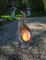 Solarleuchte Oliver in einem Garten, aus der Perspektive von vorne, mit einer leuchtenden Kugel in einer kunstvoll geschwungenen Metallhülle.