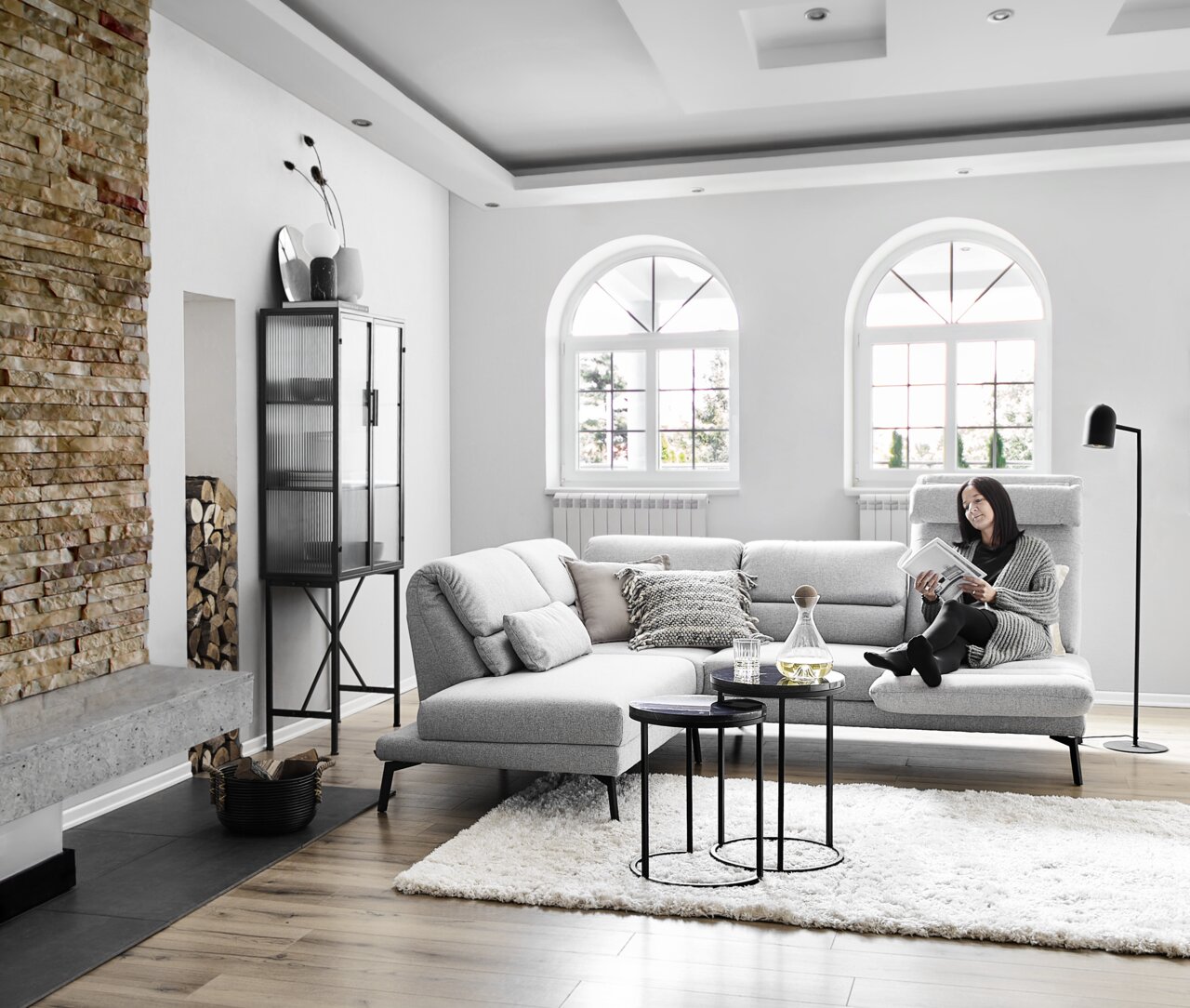 Moderne Eckgarnitur in einem stilvollen Wohnzimmer mit Blick auf eine gemütliche Leseecke, dekoriert mit Kissen und einem Beistelltisch.