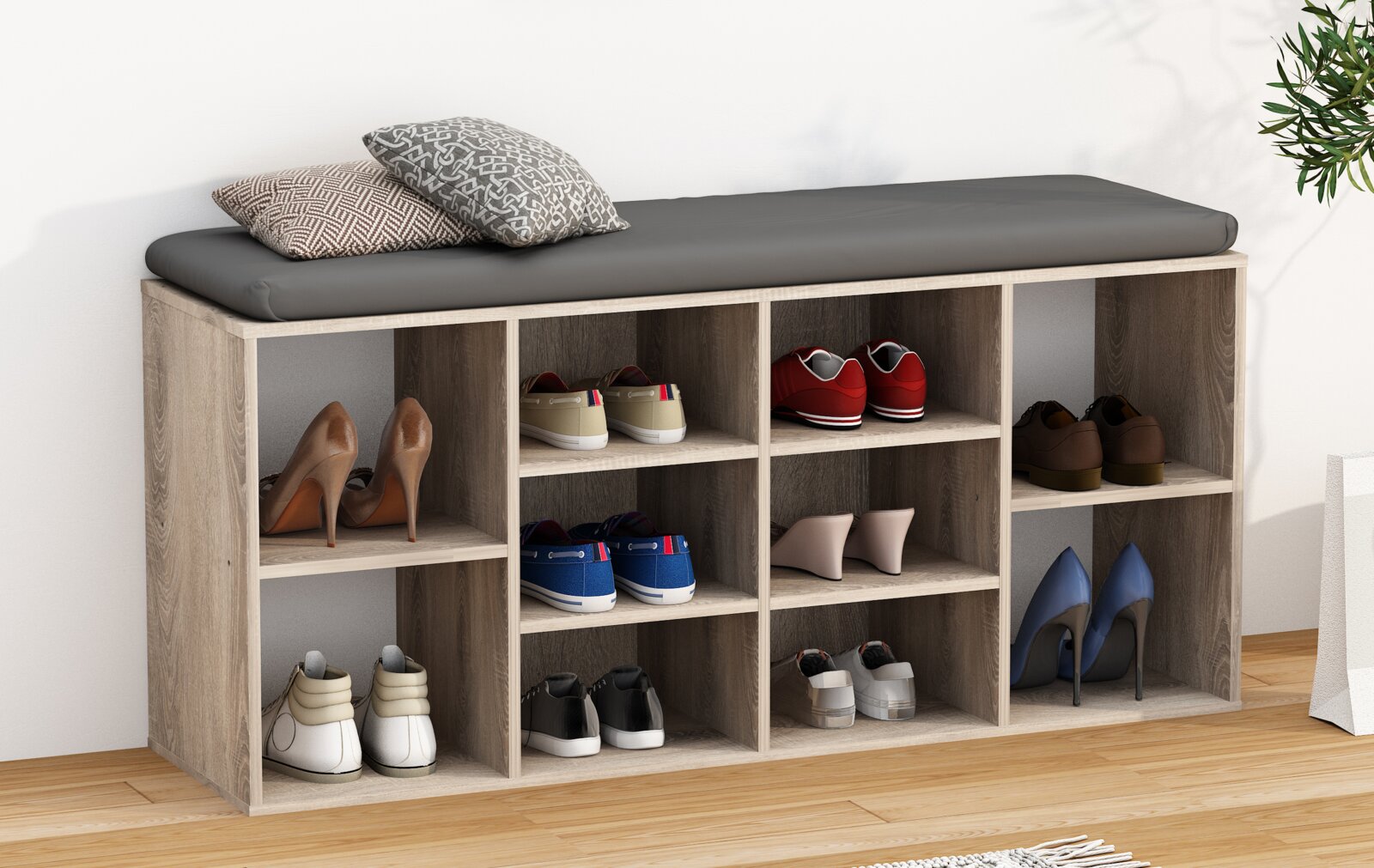 Schuhregal und Sitzbank aus hellem Holz mit grauem Sitzkissen, acht offenen Fächern und dekorativen Kissen, gefüllt mit verschiedenen Schuhpaaren; Perspektive: leicht seitliche Frontansicht von schräg oben.