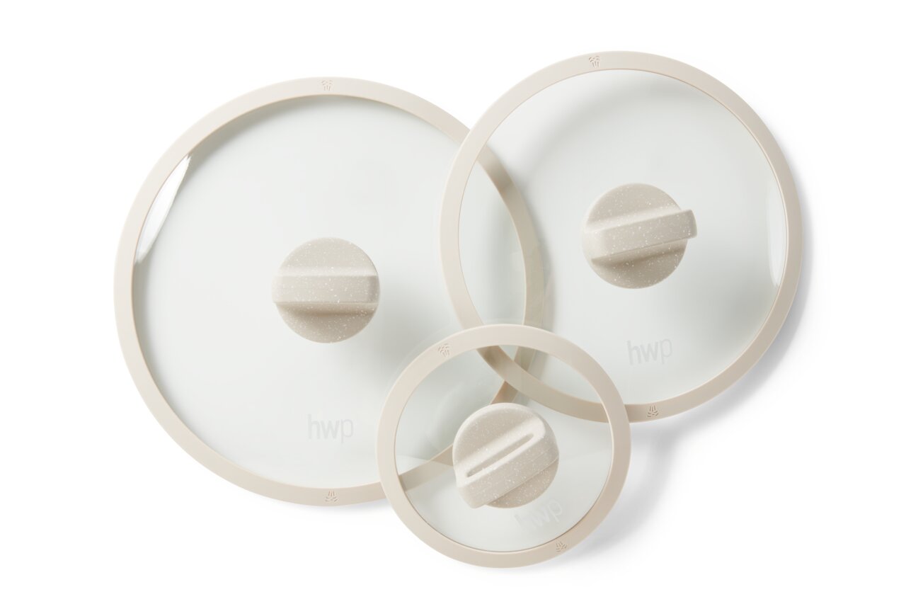 Bovenaanzicht van drie glazen deksels van verschillende grootte met een crèmekleurige rand en handvat, die deel uitmaken van een 8-delige pannenset.