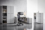 Moderner Winkelschreibtisch in einem hellen Büro, mit einem ergonomischen Bürostuhl und einem Computer, seitliche Perspektive.