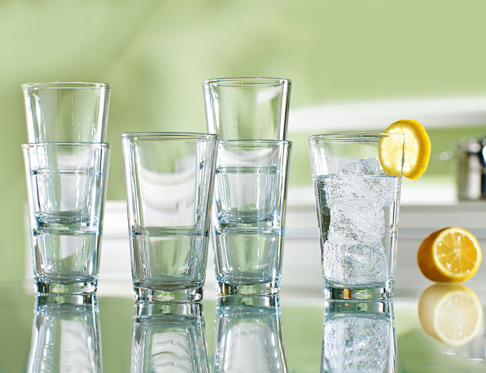 Fünf Trinkgläser Event 330ml auf einem Tisch, eines mit Eiswürfeln und Zitronenscheibe, seitliche Perspektive