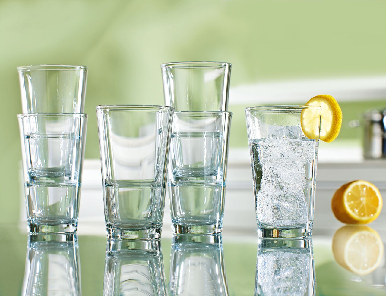 Fünf Trinkgläser Event 330ml auf einem Tisch, eines mit Eiswürfeln und Zitronenscheibe, seitliche Perspektive