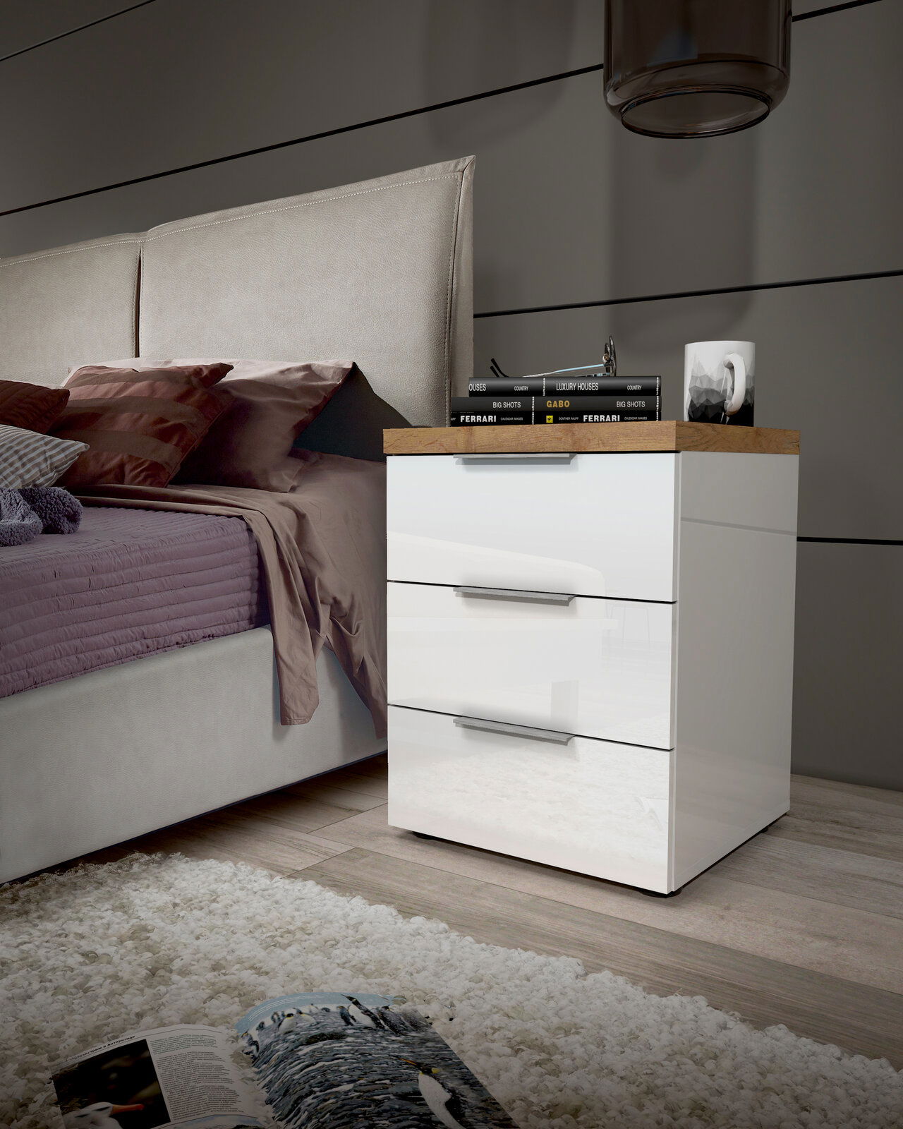 XORA Nachtkommode IDEA Moderne Nachtkommode mit drei Schubladen in Hochglanz-Weiß, seitliche Perspektive neben einem Bett, dekoriert mit Büchern und einer Lampe.