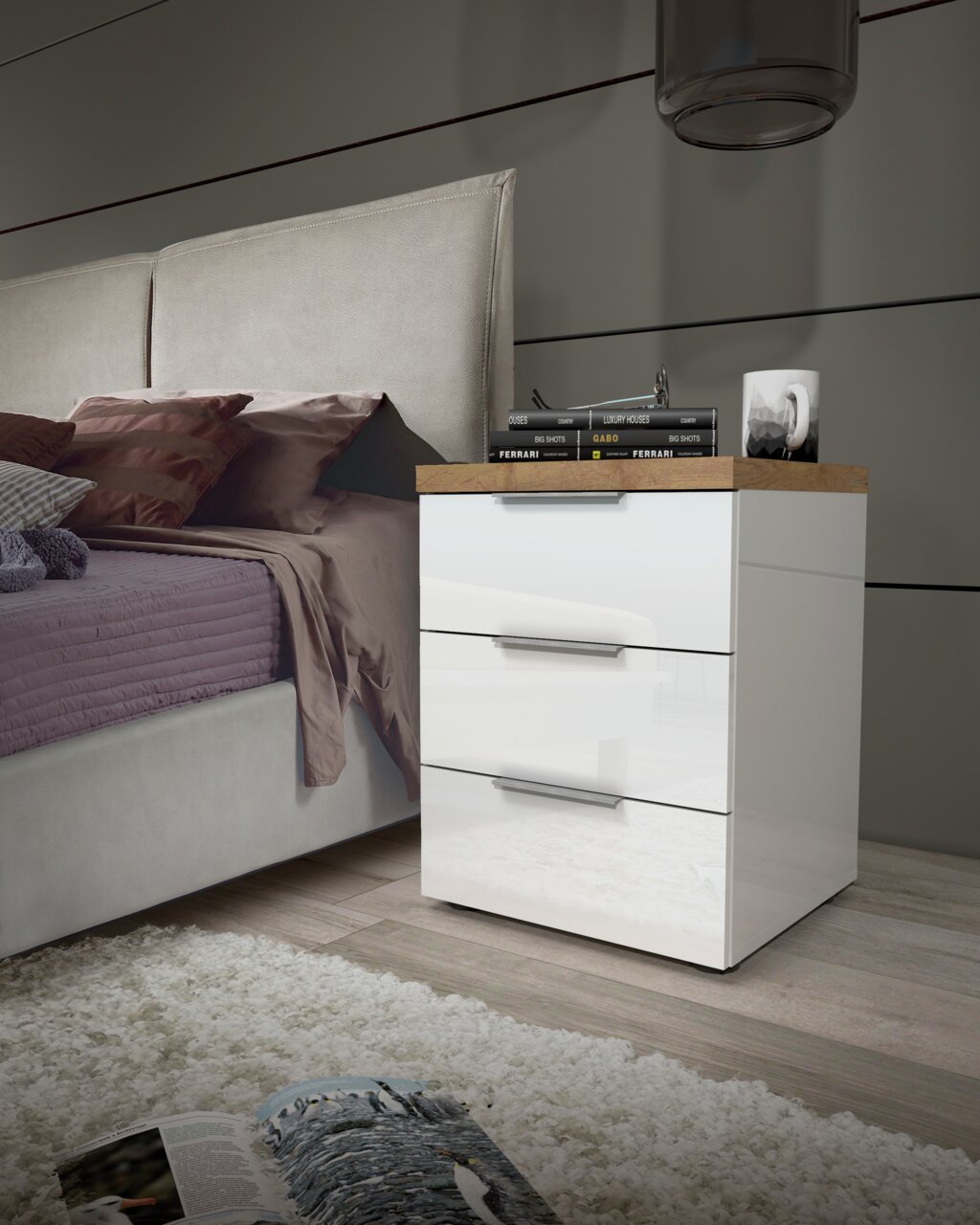 Moderne Nachtkommode mit drei Schubladen in Hochglanz-Weiß, seitliche Perspektive neben einem Bett, dekoriert mit Büchern und einer Lampe.