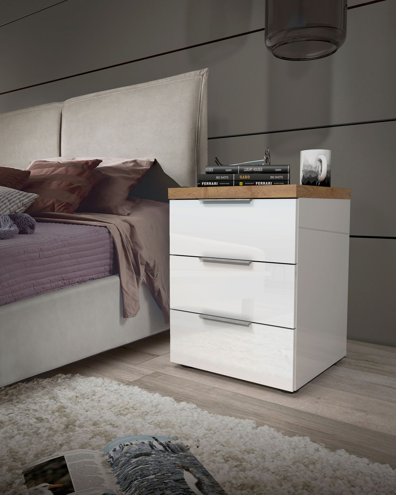 Moderne Nachtkommode mit drei Schubladen in Hochglanz-Weiß, seitliche Perspektive neben einem Bett, dekoriert mit Büchern und einer Lampe.