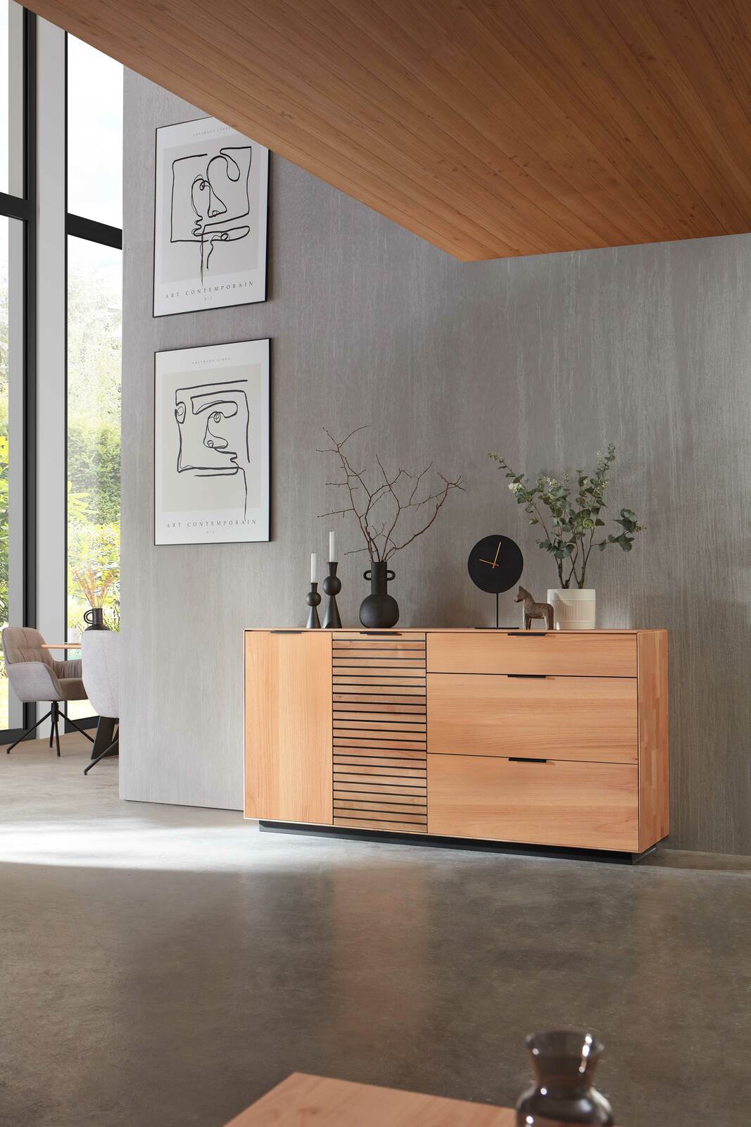 Modernes Sideboard aus Holz mit Schubladen und Lamellentür, seitliche Perspektive, dekoriert mit Vasen und Uhr.