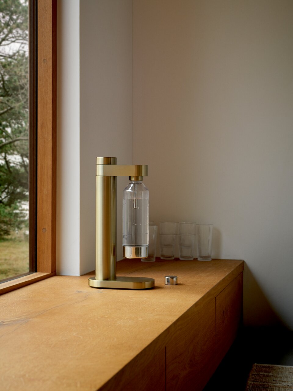 Goldener Wassersprudler auf einer Holzoberfläche, seitliche Perspektive, mit einem Fenster im Hintergrund.