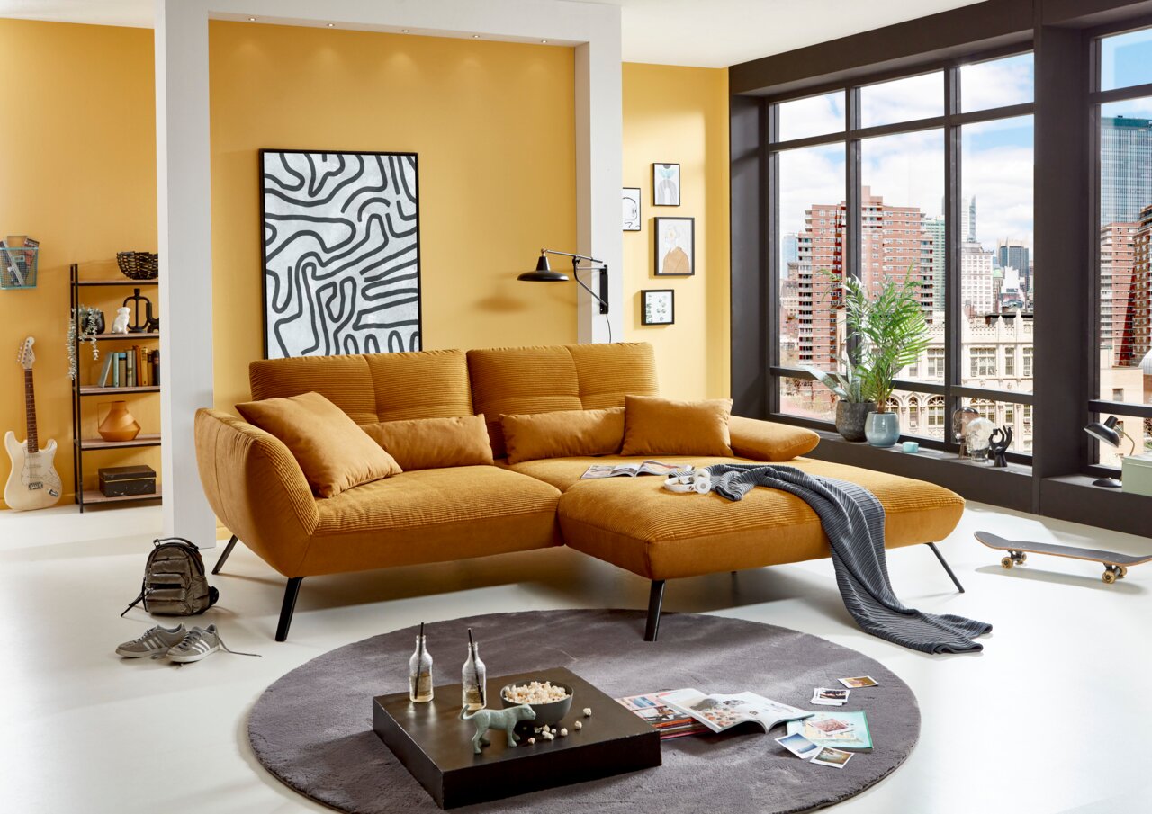 StepOne Ecksofa NEWPORT Gemütliche Rundecke in warmem Gelbton, seitliche Perspektive, in modernem Wohnzimmer mit großen Fenstern und urbanem Ausblick.