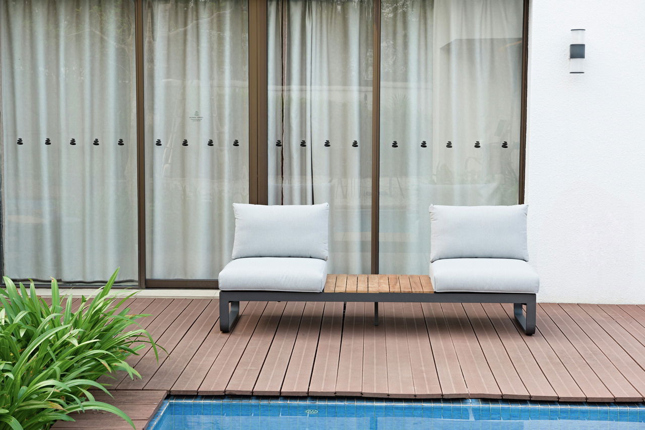 Moderne Loungeliege mit zwei weißen Kissen und einem Holztisch in der Mitte, auf einer Terrasse mit Blick auf den Pool.