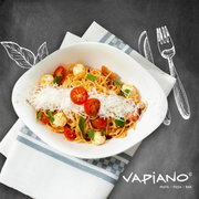 Vogelperspectief op een bord spaghetti met tomaten, mozzarella en geraspte kaas, geserveerd op een servet met het Vapiano-logo.