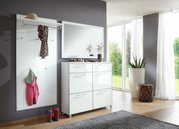 Moderner Flur mit großem rechteckigem Spiegel an der Wand, daneben eine weiße Garderobe mit Haken und Ablage, darunter eine Kommode mit glänzenden Schubladen. Perspektive von vorne mit Blick auf den hellen Raum und die großen Fenster im Hintergrund.