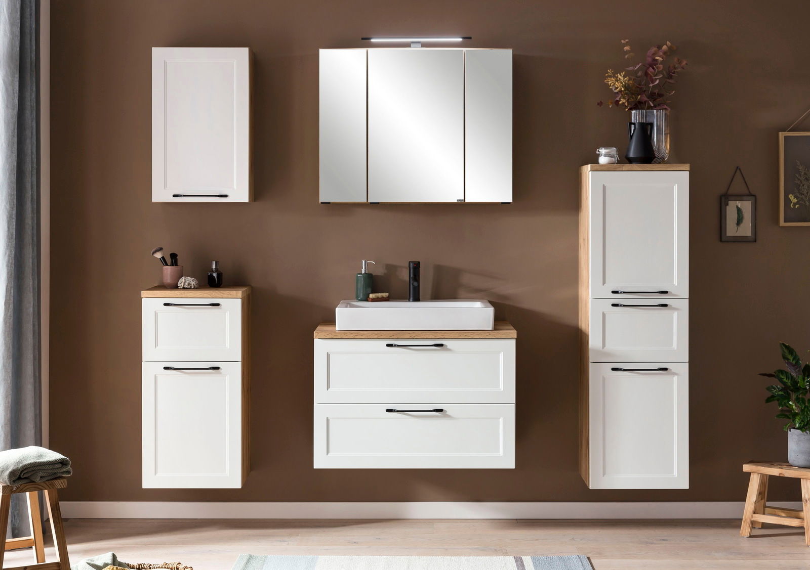Moderne Badezimmermöbel in Weiß mit Holzdetails, bestehend aus einem Midischrank, einem Waschbeckenunterschrank und einem Spiegelschrank, frontal betrachtet.