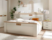 Modernes weißes Holzbett mit Eiche-Akzenten und gepolsterter Bettwäsche in hellem Schlafzimmer, aufgenommen in frontaler Perspektive mit leichtem Blick von links.