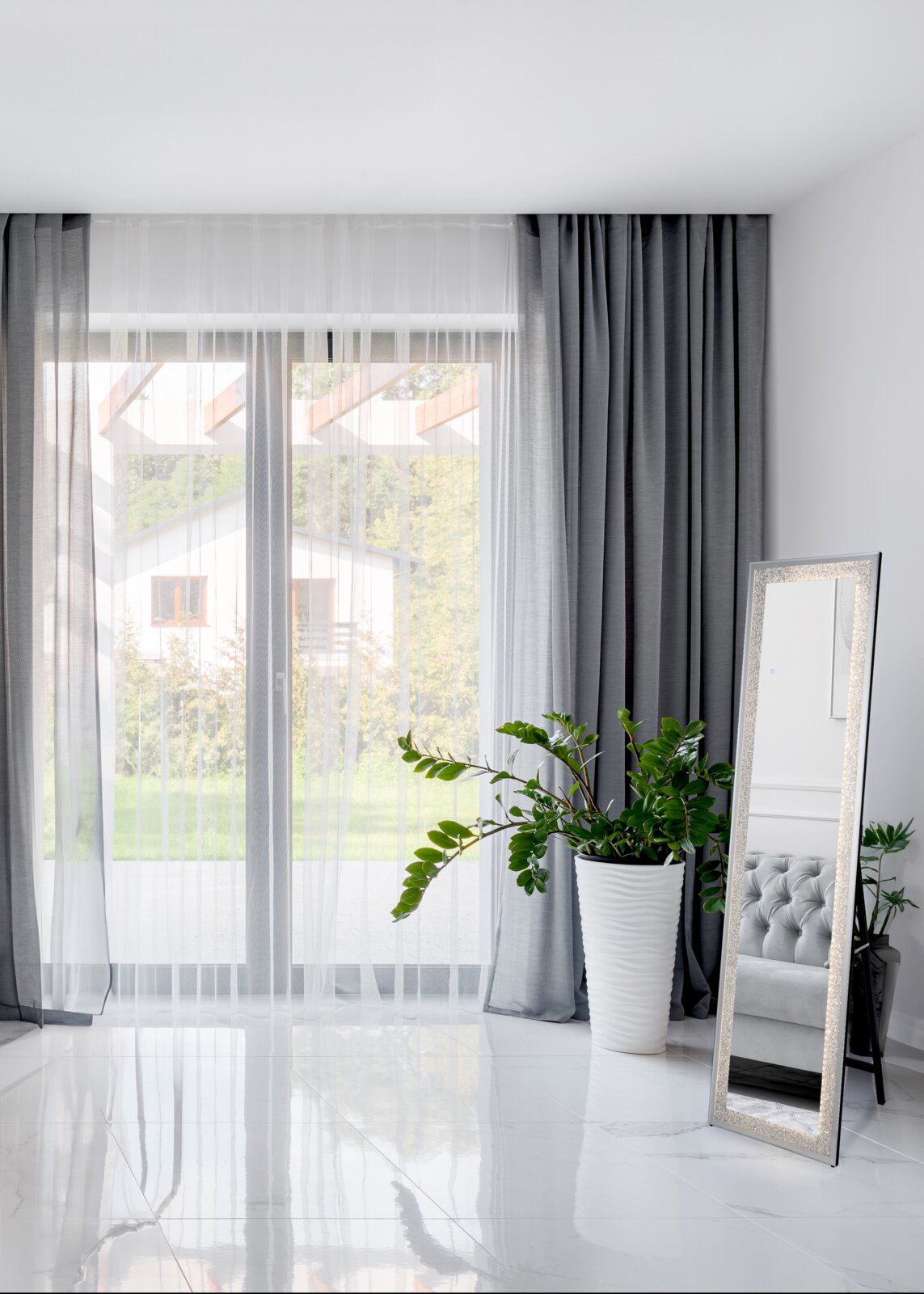 Een staande LED-spiegel van 40 x 160 cm in een moderne ruimte, schuin tegen een muur geplaatst, met een groot raam en een plantenarrangement op de achtergrond.