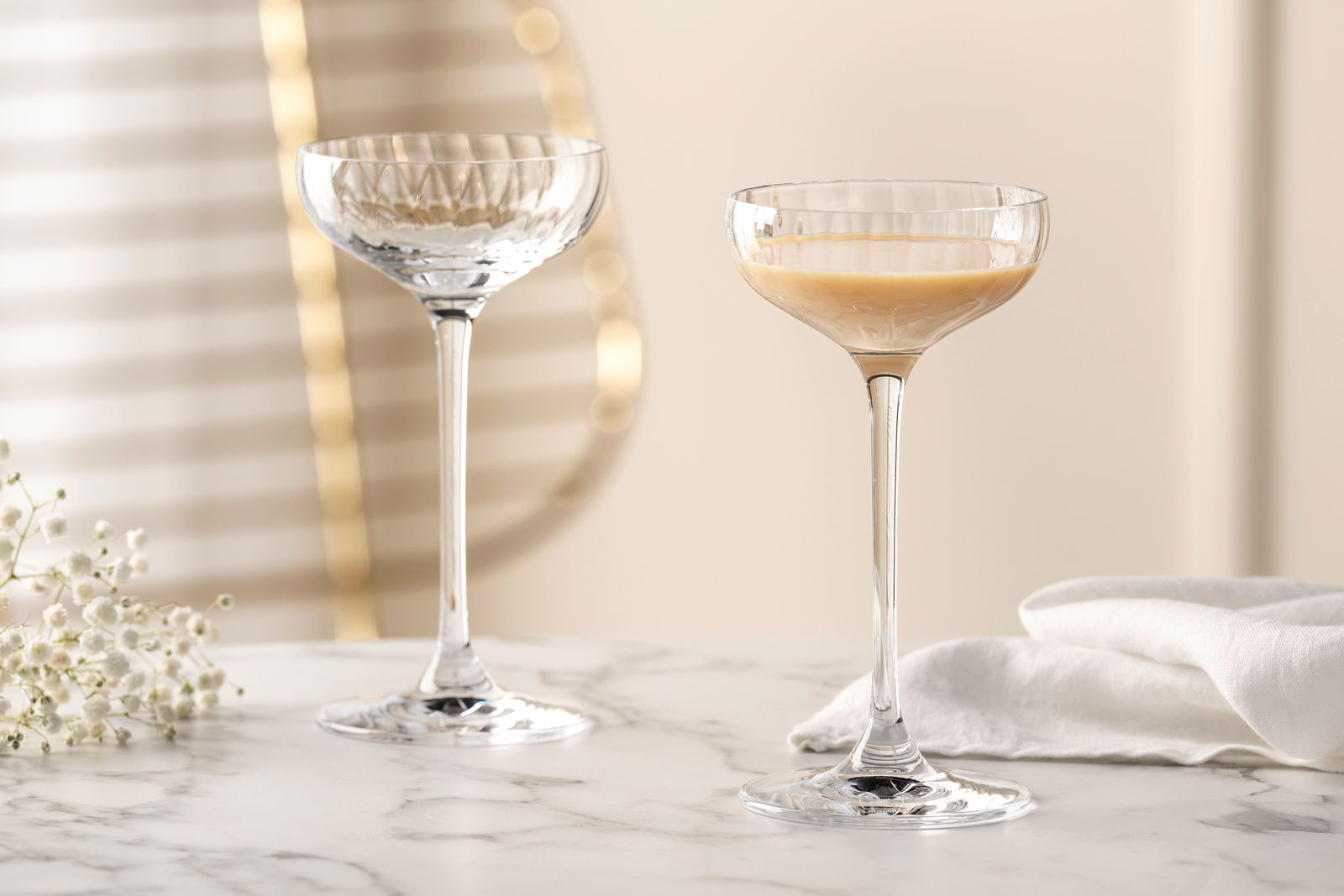 Leonardo Likörschale POESIA Zwei elegante Likörschalen aus der Serie POESIA mit 90 ml Fassungsvermögen auf einem Marmortisch, eine gefüllt mit Likör, im Hintergrund unscharfe goldene Akzente und weiße Blumen, seitliche Perspektive.