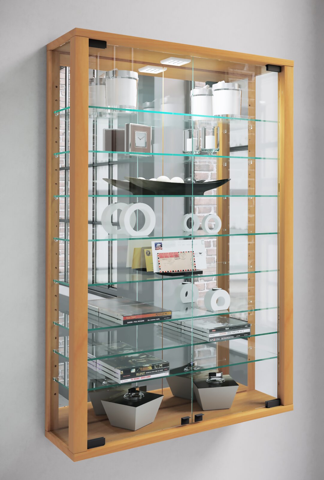 Hohe Glasvitrine mit hellem Holzrahmen, Glasböden und LED-Beleuchtung, gefüllt mit Deko-Objekten und Büchern, in schräger Frontansicht von links.