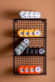 Verschiedene Tischuhren mit Kalenderfunktion in bunten Farben auf einem Gitterregal, seitliche Perspektive.