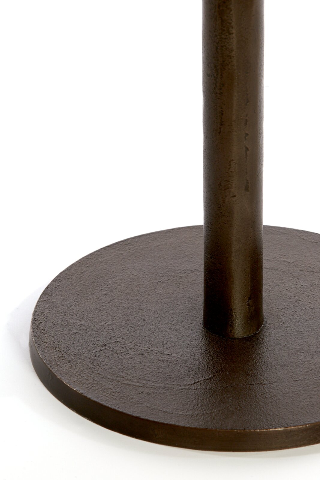 Nahaufnahme aus leicht erhöhter Perspektive auf einen runden, dunkelbraunen Metallfuß mit senkrechter Säule und rustikaler Oberfläche