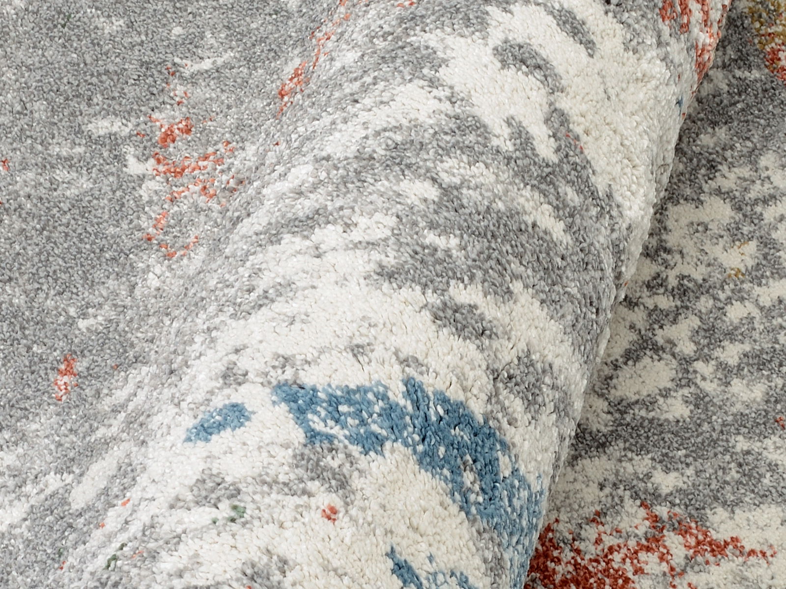 Nahaufnahme eines gerollten Frisé-Teppichs mit grauen, weißen, blauen und roten Mustern.