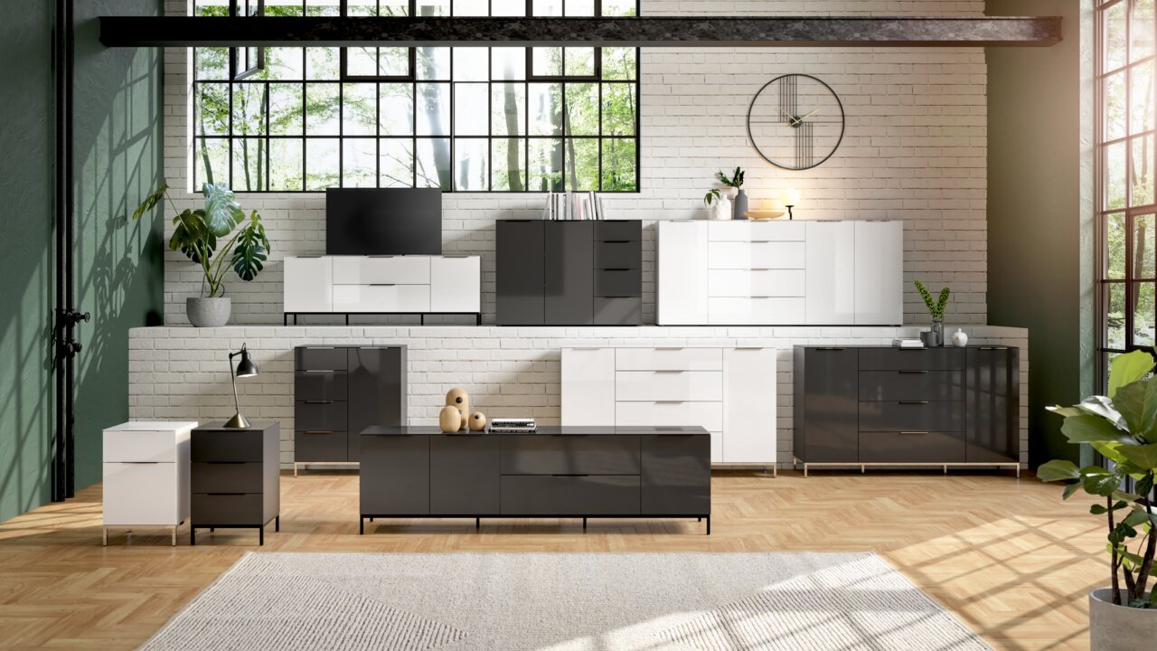 Moderne Wohnzimmermöbel in einem hellen Raum mit großen Fenstern, bestehend aus weißen und grauen Kommoden und Sideboards, frontal betrachtet.