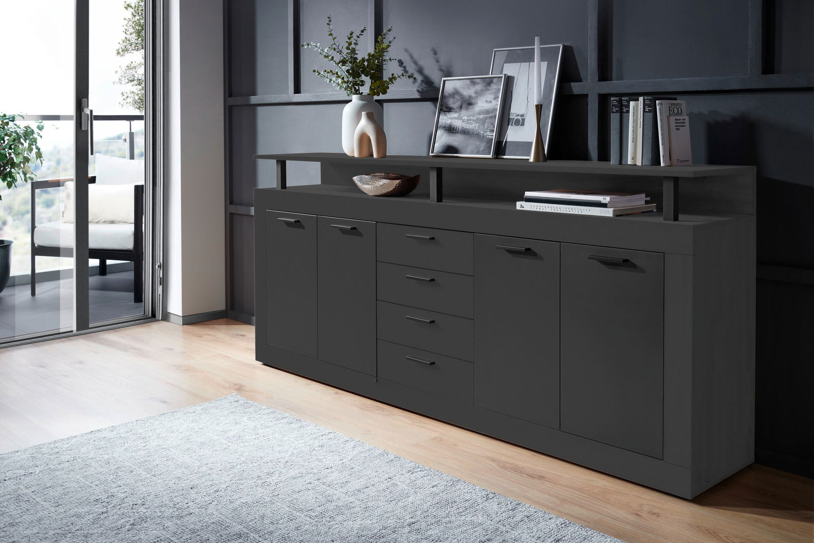 Modernes XL-Sideboard in dunklem Design, seitliche Perspektive, mit mehreren Schubladen und Türen, dekoriert mit Vasen und Büchern.