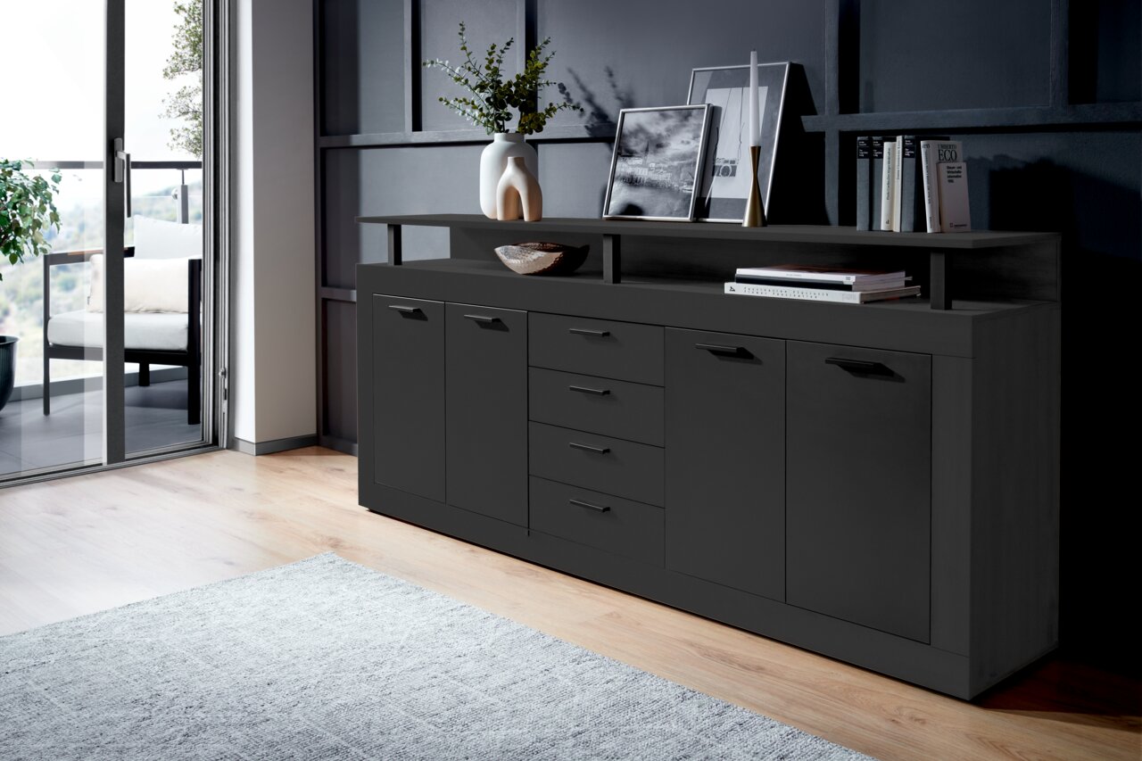 XORA XL-Sideboard MILA Modernes XL-Sideboard in dunklem Design, seitliche Perspektive, mit mehreren Schubladen und Türen, dekoriert mit Vasen und Büchern.