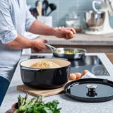 Runder Gusseisen Bräter in Schwarz mit Brot, auf einem Schneidebrett in einer modernen Küche, seitliche Perspektive.