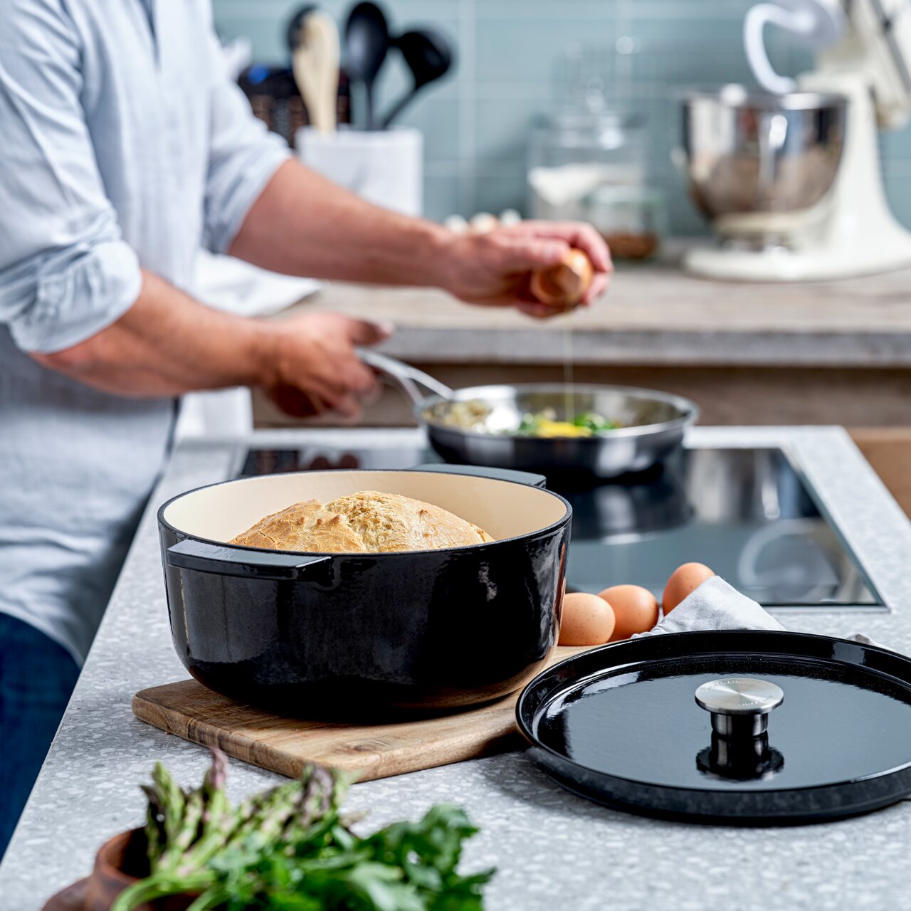 KitchenAid Bräter Runder Gusseisen Bräter in Schwarz mit Brot, auf einem Schneidebrett in einer modernen Küche, seitliche Perspektive.