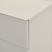 Nahaufnahme einer weißen, minimalistischen Kommode mit glatter Front und klaren Kanten, gezeigt aus schräger Perspektive von oben auf die Ecke