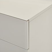 Nahaufnahme einer weißen, minimalistischen Kommode mit glatter Front und klaren Kanten, gezeigt aus schräger Perspektive von oben auf die Ecke