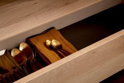 Nahaufnahme einer geöffneten Schublade aus Holz mit goldfarbenem Besteck und einem orangefarbenen Tuch, von oben betrachtet.