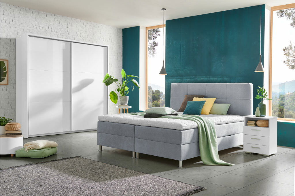 Modernes Boxbett in einem stilvollen Schlafzimmer mit grauem Polster, umgeben von Pflanzen und minimalistischen Möbeln, seitliche Perspektive.