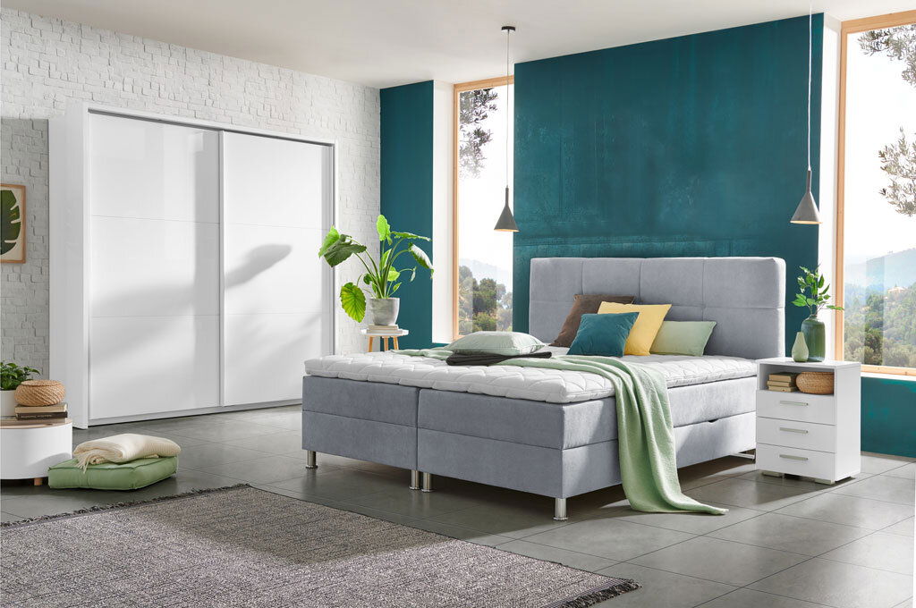 Modernes Boxbett in einem stilvollen Schlafzimmer mit grauem Polster, umgeben von Pflanzen und minimalistischen Möbeln, seitliche Perspektive.